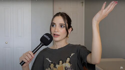 Woman holding microphone during an indoor interview or presentation, gesturing with raised hand.