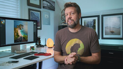 Photographer in a studio speaking toward camera while wearing a graphic t-shirt.