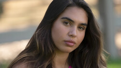 Young woman with long dark hair looking directly at camera with neutral expression.