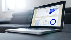Laptop displaying a dashboard with data visualizations including charts, graphs, and a blue pie chart.