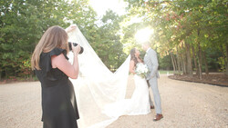 Wedding photographer capturing bride and groom on tree-lined path during golden hour.