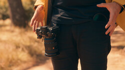 Photographer holding a mirrorless camera with telephoto lens during golden hour outdoor shoot.