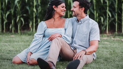 Couple sitting together on grass with cornfield in background, both wearing light blue shirts and smiling at each other.