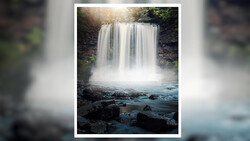 Waterfall cascading over dark rocky cliff with mist and turquoise pool below, surrounded by green forest.