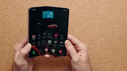 Hands holding a foldable smartphone with dark interface displaying app icons and a red car image.