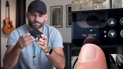 Man in gray shirt and cap demonstrating a small device with his hands while a smartphone screen shows 'No signal' message.