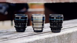 Three vintage cinema lenses arranged in a row on a wooden surface, displaying blue, silver, and blue lens barrels with manual focus rings.