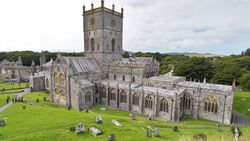 Medieval stone cathedral with square tower surrounded by green lawn and gravestones.