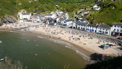 Aerial view of a crowded beach cove with seaside buildings and boats in shallow water.