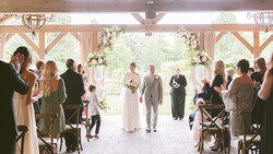 Bride and groom walk down the aisle during a wedding ceremony in a rustic timber-frame venue with guests seated on both sides.
