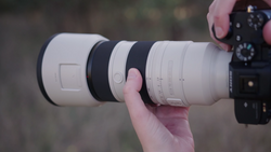 Photographer holding a white telephoto lens attached to a camera body with visible focus ring and depth-of-field markings.