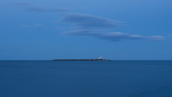 Cargo ship on the horizon under a blue sky with wispy clouds and calm sea.