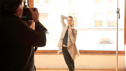 Photographer shooting a portrait of a woman posing in a bright studio with large windows.