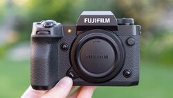 Fujifilm X-H2S mirrorless camera body held in hand against blurred green background.