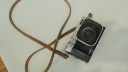 Vintage rangefinder camera with black body and chrome details, attached to a brown leather shoulder strap.