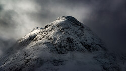 Snow-covered mountain peak shrouded in dramatic storm clouds and mist.