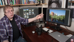 Photographer at desk with dual monitors showing photo editing software and a camera.
