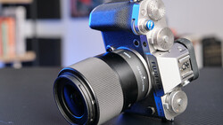 Mirrorless camera with blue and black body paired with a prime lens on dark surface.