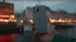 Hand holding iPhone 12 Pro with triple camera setup against blurred evening cityscape with warm lights.