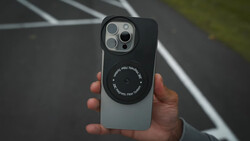 Hand holding iPhone 14 Pro with magnetic ring attachment and camera lens protector visible.