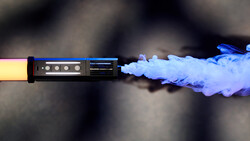 Yellow-gripped device emitting blue vapor against a dark blurred background.