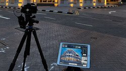 Professional camera on tripod pointed at tablet displaying architectural photograph on urban street at dusk.