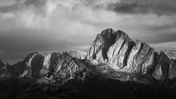 Dramatic black and white mountain landscape with jagged peaks and stormy sky overhead.