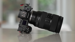 Mirrorless camera with telephoto lens mounted, displayed at a slight angle on a reflective surface.