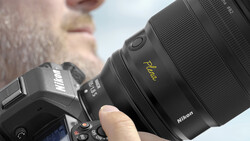 Photographer holding a Nikon camera with a prime lens featuring a gold nameplate marking.