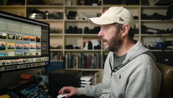 Photographer working at a computer with photo editing software and color reference tools displayed on monitor.