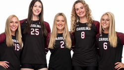 Five volleyball players in black uniforms with Carolina branding posed together for a team portrait.