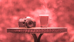 Vintage rangefinder camera and glass of red juice on decorative table against pink bokeh background.