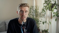 Man wearing glasses and dark shirt speaking into microphone during interview or podcast recording.