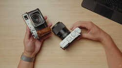 Hands holding two vintage rangefinder cameras with interchangeable lenses on a wooden desk.