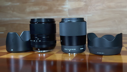 Four camera lenses with their hoods arranged in a row on a wooden surface.