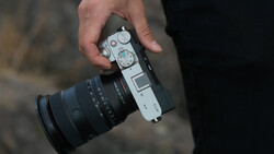 Photographer's hand holding a rangefinder camera with attached telephoto lens.