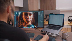 Photographer working at desk with external monitor displaying portrait editing in progress.