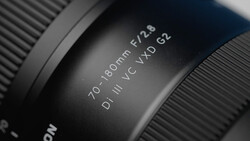 Close-up of camera lens barrel showing 70-180mm focal length and f/2.6 aperture specifications.