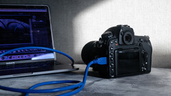 Professional camera connected via blue USB cable to laptop displaying image editing software.