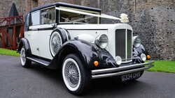 Vintage two-tone convertible automobile with white upper body and black lower body parked on asphalt.