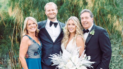 Bride and groom pose with two adults in formal attire against a willow tree backdrop.