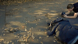 Photographer lying on pavement composing a low-angle shot of a person in blue jacket.