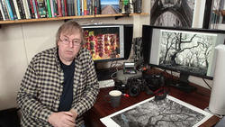 Photographer at desk surrounded by cameras, monitors displaying landscape images, and film prints.