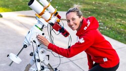 Woman in red jacket posing with a white telescope mounted on an equatorial tracking mount.