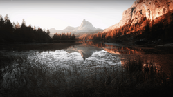 Alpine lake with mirrored reflections of forested peaks and rocky cliffs at golden hour.