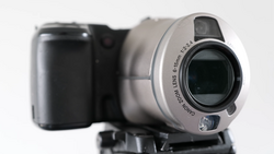 Silver camcorder with black handle shown alongside blurred dark compact camera against white background.
