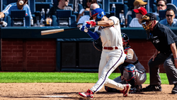Baseball batter mid-swing during day game with catcher and umpire behind home plate.
