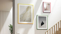 Three framed artworks displayed on a white wall beside a wooden staircase.