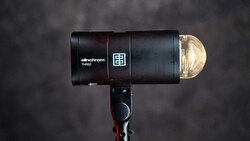 Elinchrom THREE monolight with reflector dome positioned against a dark textured backdrop.