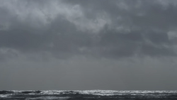Turbulent ocean waves under heavy gray storm clouds at horizon.